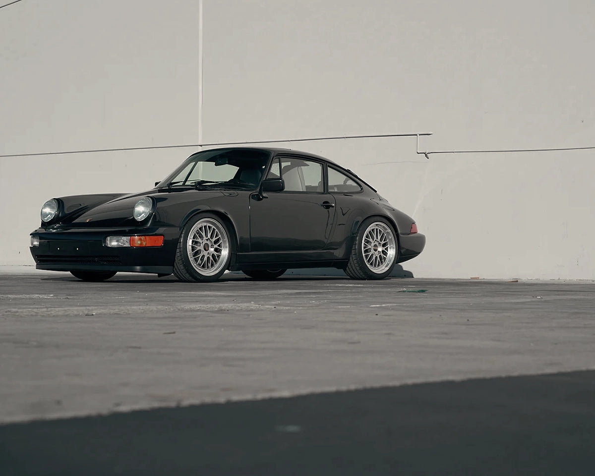 Black Porsche 911 964 narrow body on staggered 18-inch silver BBS LM wheels, photographed from the front.
